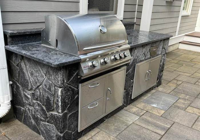 Stone-clad outdoor kitchen island with built-in grill and granite counter